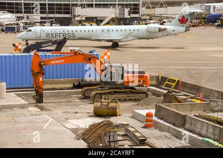 SEATTLE TACOMA AIRPORT, WA, USA - JUNE 2018: Excavator at Seattle Tacoma airport being used on construction work. An Air Canada Express jet is taxiing