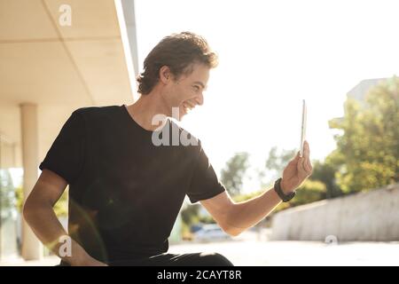 Cheerful young man using tablet for video chat at university campus on sunny day Stock Photo