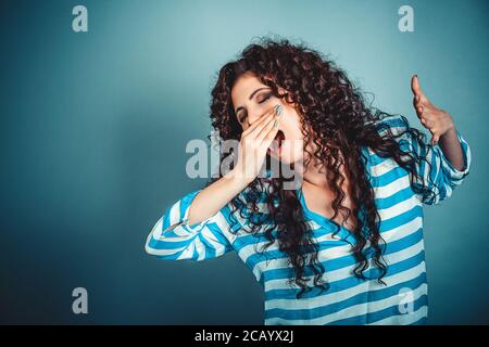 It is too early for me. Closeup portrait sleepy young woman with wide open mouth yawning eyes closed looking bored isolated blue wall background. Face Stock Photo