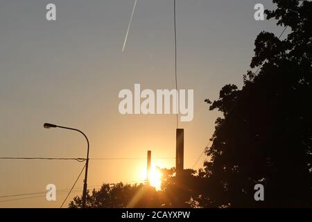 The sun sets - you see this from Palmovka, Prague. You can see a chimney in the distance. There is a contrail in the sky, from a passing aeroplane. Stock Photo