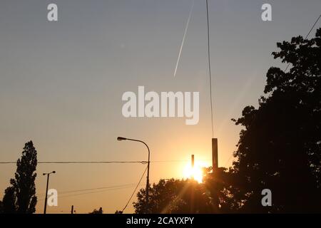 The sun sets - you see this from Palmovka, Prague. You can see a chimney in the distance. There is a contrail in the sky, from a passing aeroplane. Stock Photo