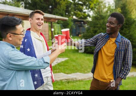 Waist up portrait of multi-ethnic group of men drinking beer while enjoying outdoor party in Summer for Independence day Stock Photo