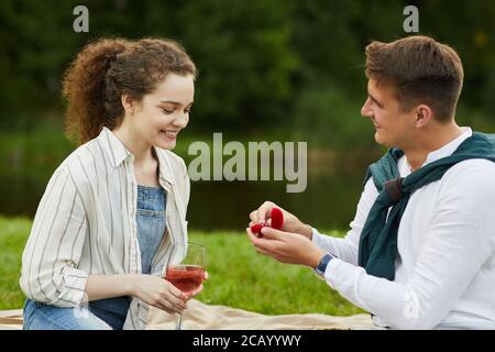 Side view at young man opening ring box while proposing to girlfriend during romantic date outdoors Stock Photo