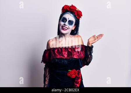 Young woman wearing mexican day of the dead makeup smiling cheerful presenting and pointing with palm of hand looking at the camera. Stock Photo