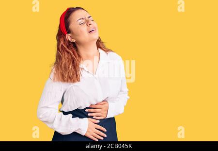 Young latin woman wearing waitress apron with hand on stomach because nausea, painful disease feeling unwell. ache concept. Stock Photo