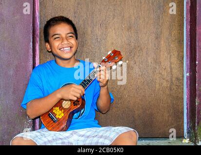 Local boy plays his ukulele. The ukulele is a popular musical instrument on Kosrae, Micronesia, as it is on many Pacific islands. Stock Photo