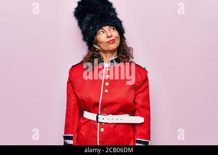 Middle age beautiful wales guard woman wearing traditional uniform over pink background smiling looking to the side and staring away thinking. Stock Photo