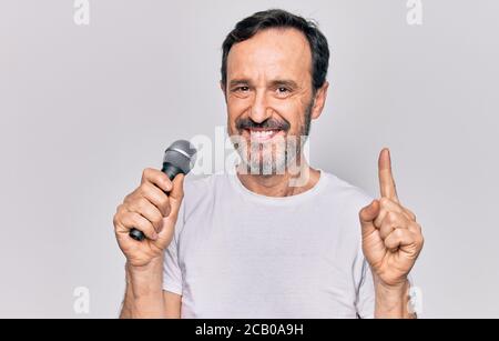 Middle age handsome singer man singing using microphone over isolated white background smiling with an idea or question pointing finger with happy fac Stock Photo