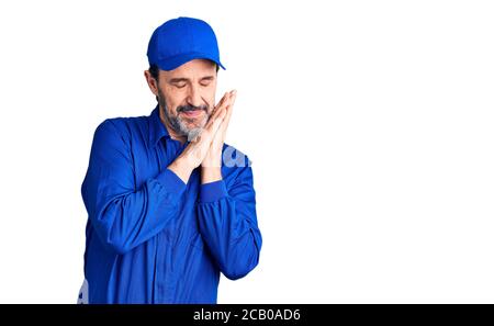 Middle age handsome man wearing mechanic uniform sleeping tired dreaming and posing with hands together while smiling with closed eyes. Stock Photo