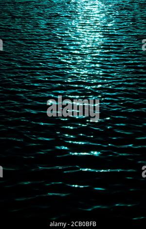 Ripples of water surface with sun reflections, dark tone image with high contrast and blue filter, vertical frame. Stock Photo