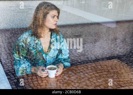 A young beautiful woman drinking a cappuccino all alone in a local coffee shop in the city of Lisbon, Portugal