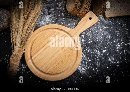 An empty wooden cutting board and wheat on the table with bread. Stock Photo