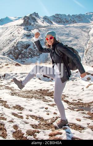 A young girl in glasses dances on the snow. Mountains in the winter. Stock Photo