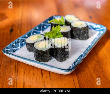 Mini Avocado Sushi Rolls on a rectangular plate and wooden table background blur Stock Photo