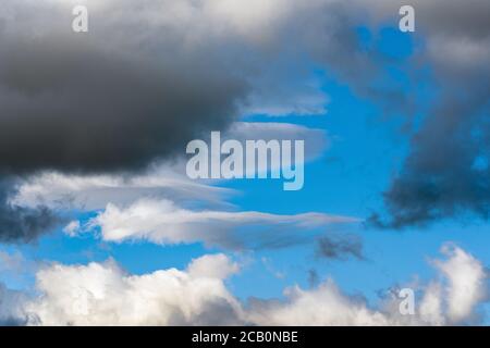 White clouds and dramatic dark thunderclouds floating across blue sky to change season weather. View of natural meteorology background landscape. Stock Photo
