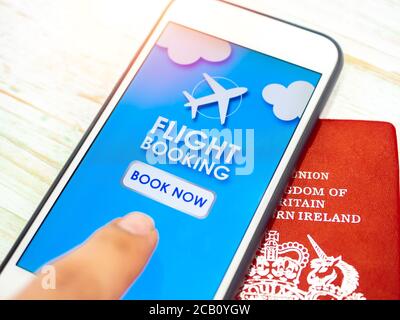 Close-up flight booking online on application on smartphone with red passport on white vintage wooden plank. Finger pressing on book now button on mob Stock Photo