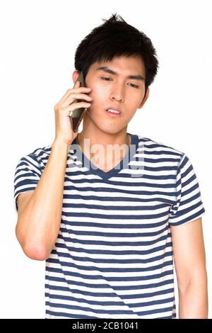 Studio shot of young handsome Asian man talking on mobile phone isolated against white background Stock Photo