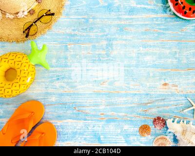 Colorful beach accessories, seashells, straw hat, sunglasses, orange flip flops and aerated beach ball on vintage blue wooden plank with space. Travel Stock Photo