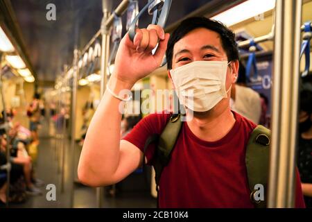 young adult Asian man wearing a face mask on subway train in Bangkok, Thailand. New normal lifestyle during Covid19 - Coronavirus pandemic Stock Photo