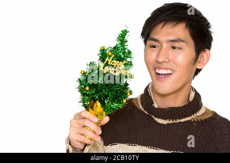 Studio shot of young handsome Asian man holding Happy New Year tree and smiling isolated against white background Stock Photo