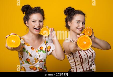 Caucasian twins with curly hair posing with oranges in hand on a yellow studio wall Stock Photo