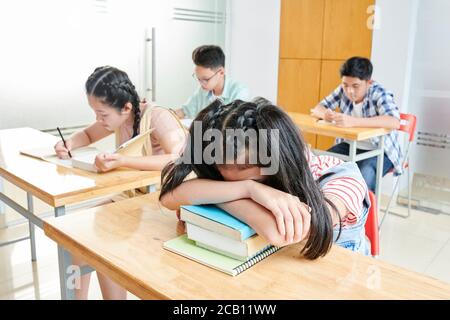 Tired girl leaning on students books, she and other shool students stayed after classes to do homework and work on projects Stock Photo