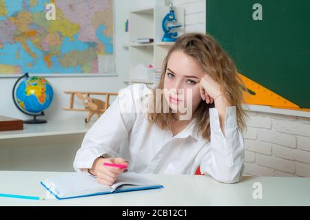 Teenage student. Portrait of a pensive young girl making notes while sitting with books. Stock Photo