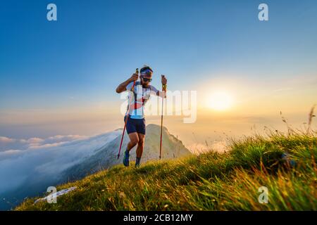 Man with poles in the mountains with sunset behind Stock Photo
