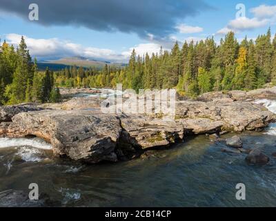 Beautiful northern landscape with wild glacial river Kamajokk, boulders and spruce tree forest in Kvikkjokk in Swedish Lapland. Summer sunny day Stock Photo