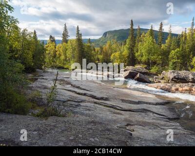 Beautiful northern landscape with wild glacier river Kamajokk, boulders and spruce tree forest in Kvikkjokk in Swedish Lapland. Summer sunny day Stock Photo