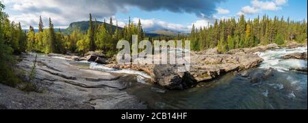 Beautiful wide panoramic landscape with wild glacier river Kamajokk, boulders and spruce tree forest in Kvikkjokk in Swedish Lapland. Summer sunny day Stock Photo