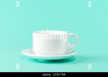 Empty porcelain coffee cup and a saucer over a mint green color background. White ceramic teacup. Modern stylish tableware. Copy space. Front view. Stock Photo
