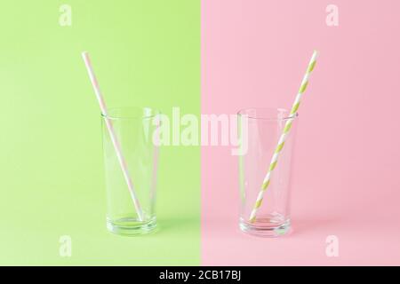 Empty tall glass with a pink paper drinking straw on a green background and one more with a green paper drinking straw on a pink background. Stock Photo