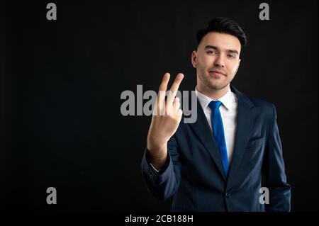 Portrait of business man wearing blue business suit and tie showing two fingers isolated on black background with copy space advertising area Stock Photo