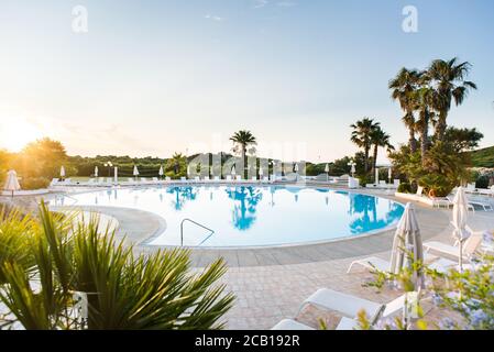 Water Pool with Sunbeds, Umbrellas and Palms. Luxury Panoramic View. Sardinia. Italy. Sunrise. Stock Photo