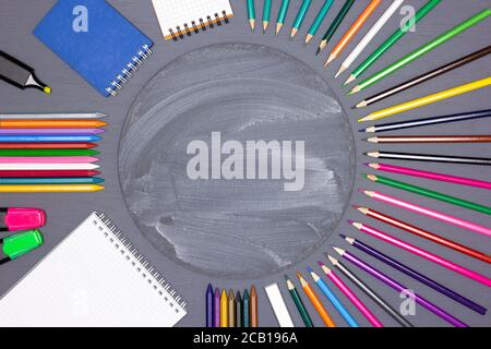 Blank notebooks, markers, colored pencils, chalk stick with round chalkboard on desk. Children's creativity, back to school concept background Stock Photo