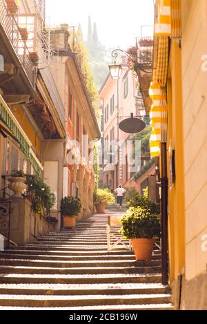 Sunrise on Old Picturesque Street in Bellagio City. Lombardy. Italy. Early Morning without Tourists. Woman Go Up on Staircase. Stock Photo