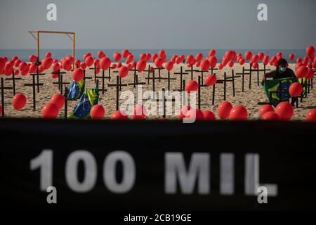 Rio De Janeiro, Brazil. 08th Aug, 2020. An employee of the non-governmental organisation 'Rio de Paz' attaches a Brazilian flag to a cross. The NGO has placed 1000 red balloons and 100 crosses on Copacabana beach in memory of the victims of the Covid 19 pandemic. Credit: Fernando Souza/dpa/Alamy Live News Stock Photo