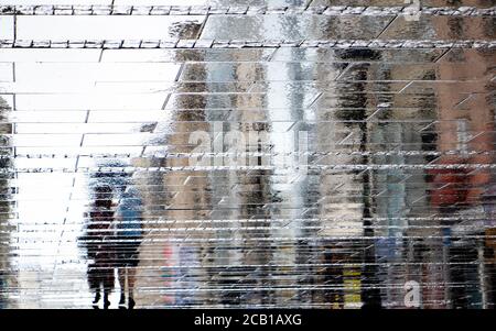 Blurry reflection shadow silhouette on wet puddle of a couple walking a city street on a rainy day, abstract background Stock Photo