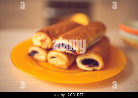Buns with black currant jam in orange plate on a wooden table. Background tea cup and oven Stock Photo