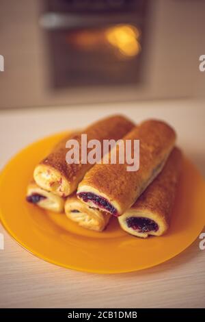 Buns with black currant jam in orange plate on the kitchen table. Background turned oven Stock Photo