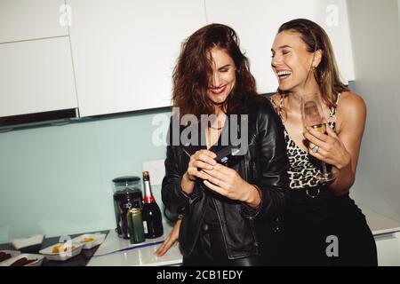 Happy women friends having fun partying at home. Smiling women drinking wine and taking photos at home. Stock Photo