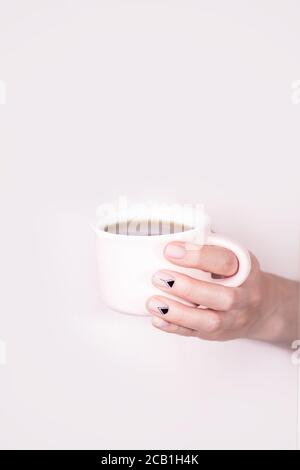 Female hands holding pink cup of black tea on pink background. Natural manicure with triangles pattern Stock Photo