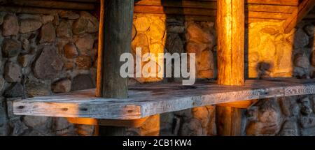 wooden table against the background of a stone wall illuminated by the warm natural light of the setting sun Stock Photo