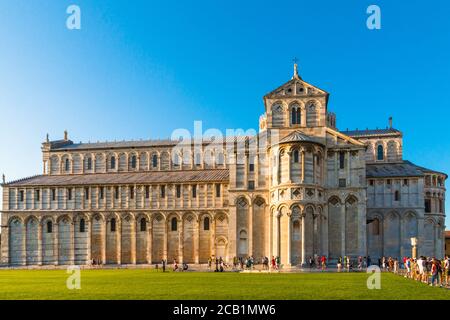 Perfect sideview of the historic medieval Pisa Cathedral (Duomo di Pisa) with a nice green lawn in front, a blue sky in the background and people... Stock Photo