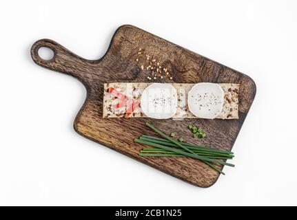 Crispbread topped with goat cheese on wooden cutting board Stock Photo