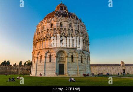 Magnificent landscape shot of the famous Pisa Baptistery of St. John. People are sitting on the lawn in front of the Roman Catholic ecclesiastical ... Stock Photo