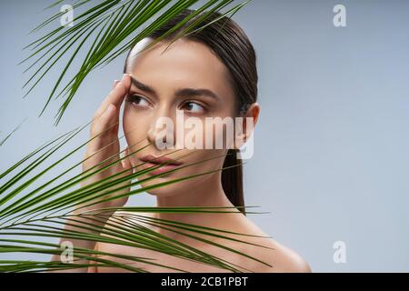 Charming young woman standing behind green plant Stock Photo