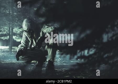 Man In Full Biohazard Protective Suit Gloves And Gas Mask Inspecting Soil In Wooded Area. Stock Photo