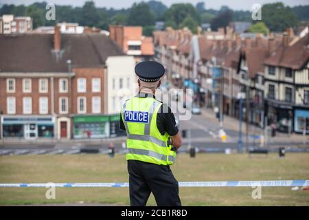 policeman stands guard at cordon at crime scene overlooking English town Stock Photo